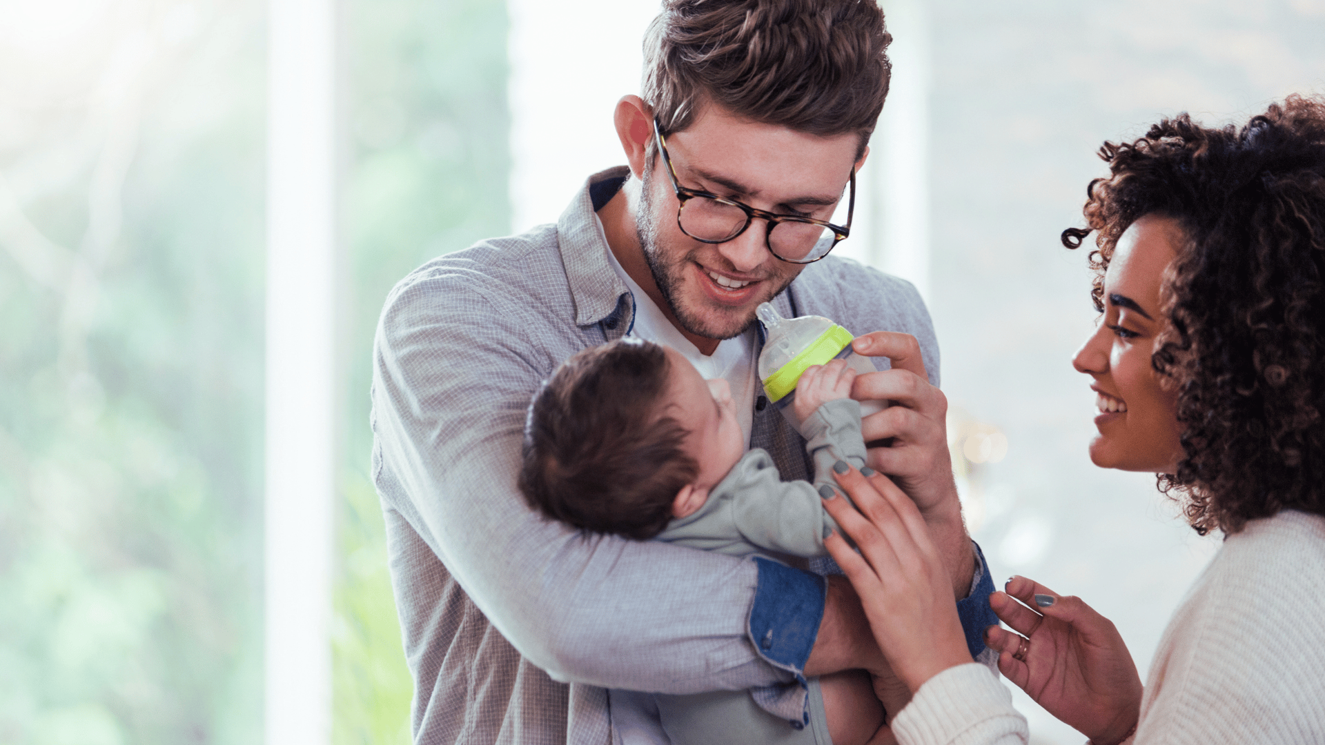 A man and woman smile while holding a baby together, showcasing a moment of joy and connection.