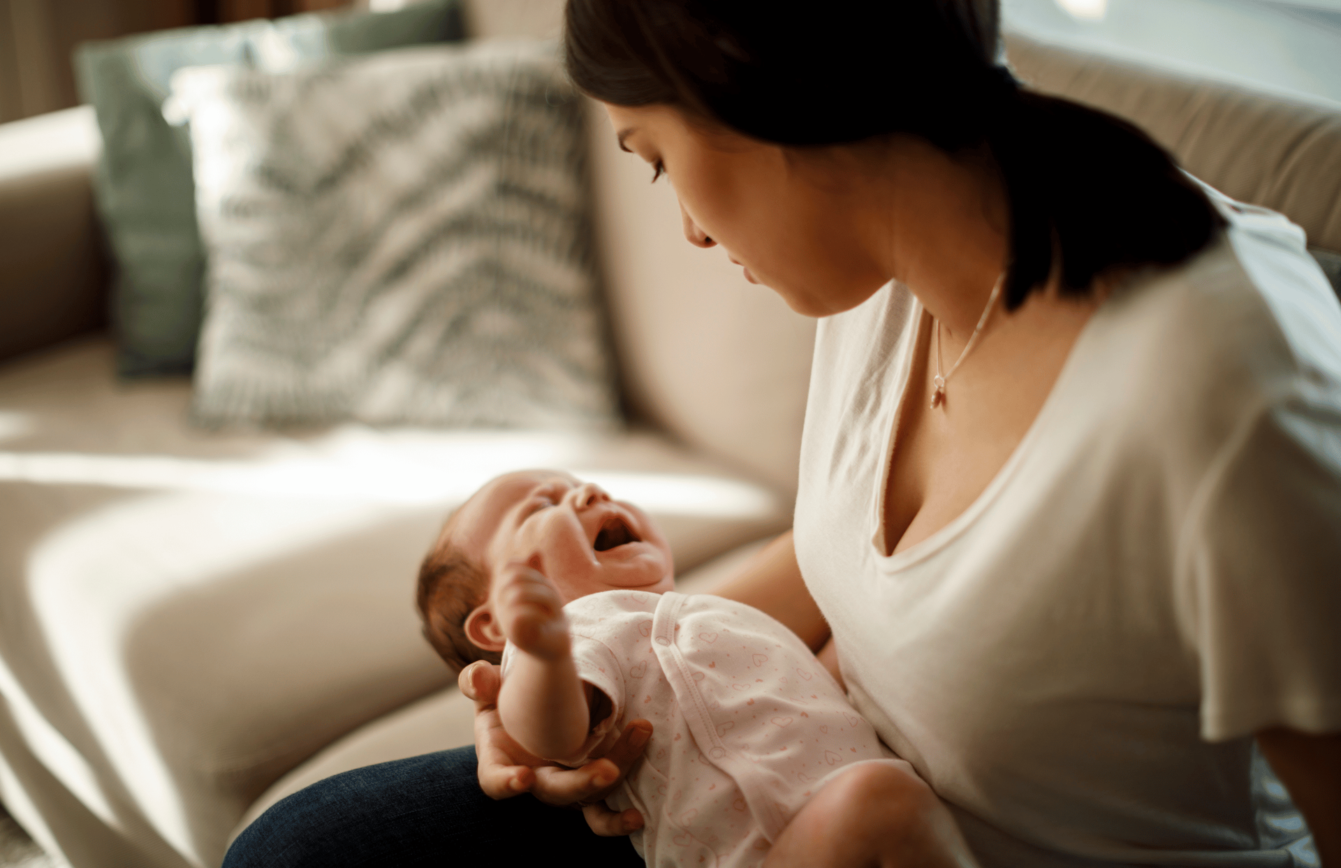A woman sits on a sofa holding a crying baby in her arms.