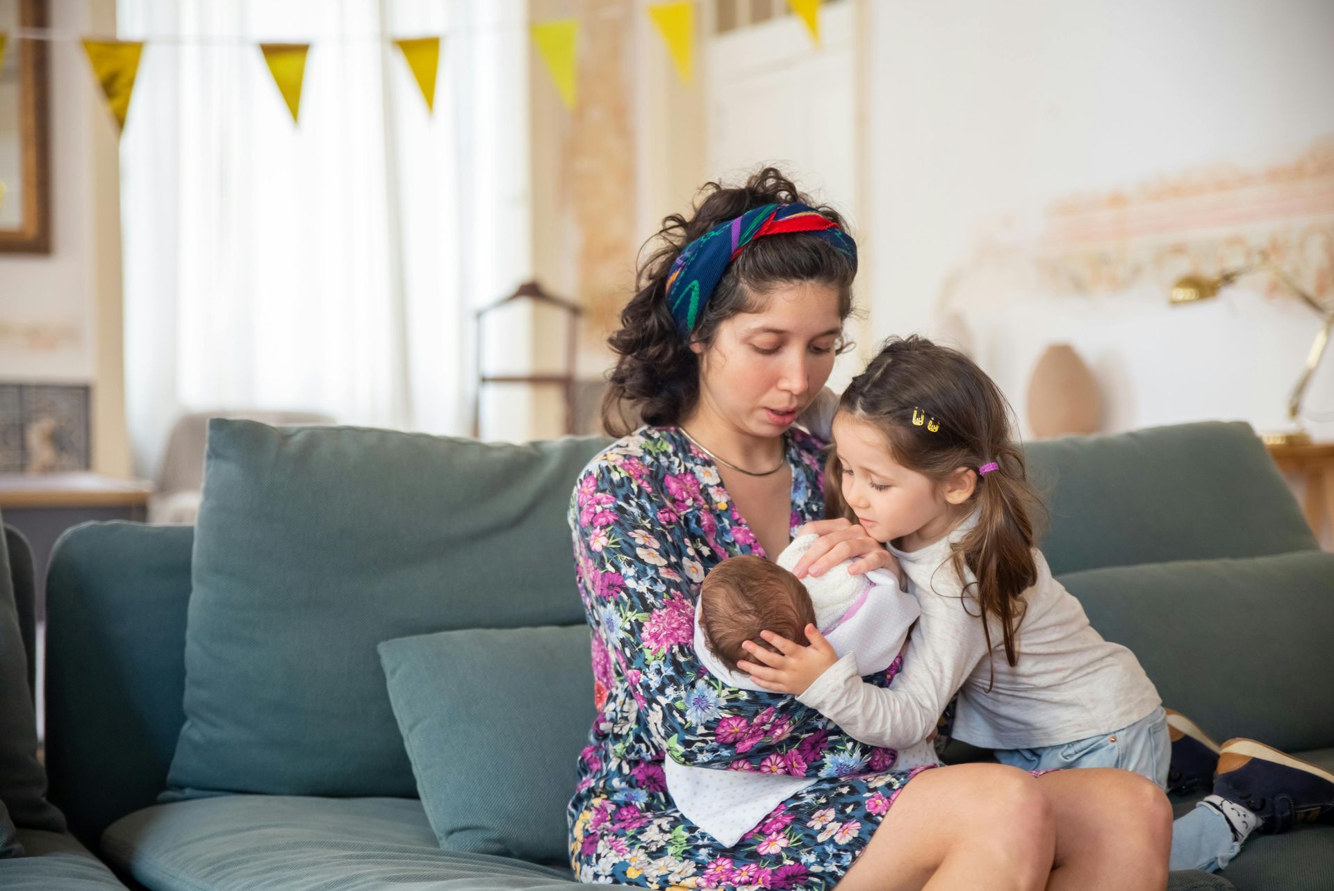 A mother holds her newborn while her older daughter looks over her newborn