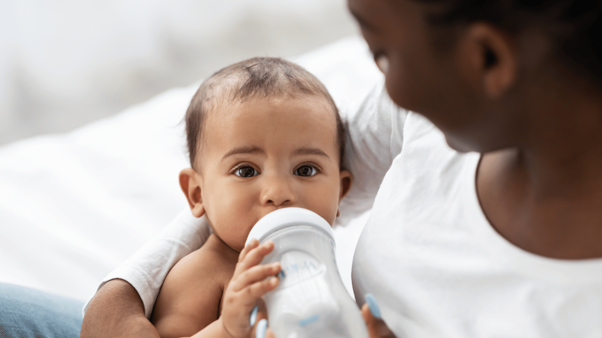 A woman gently feeds her baby with a bottle, showcasing a nurturing moment between mother and child.