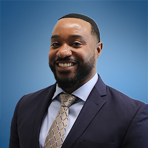 Man in a suit smiles, against a wooden background.