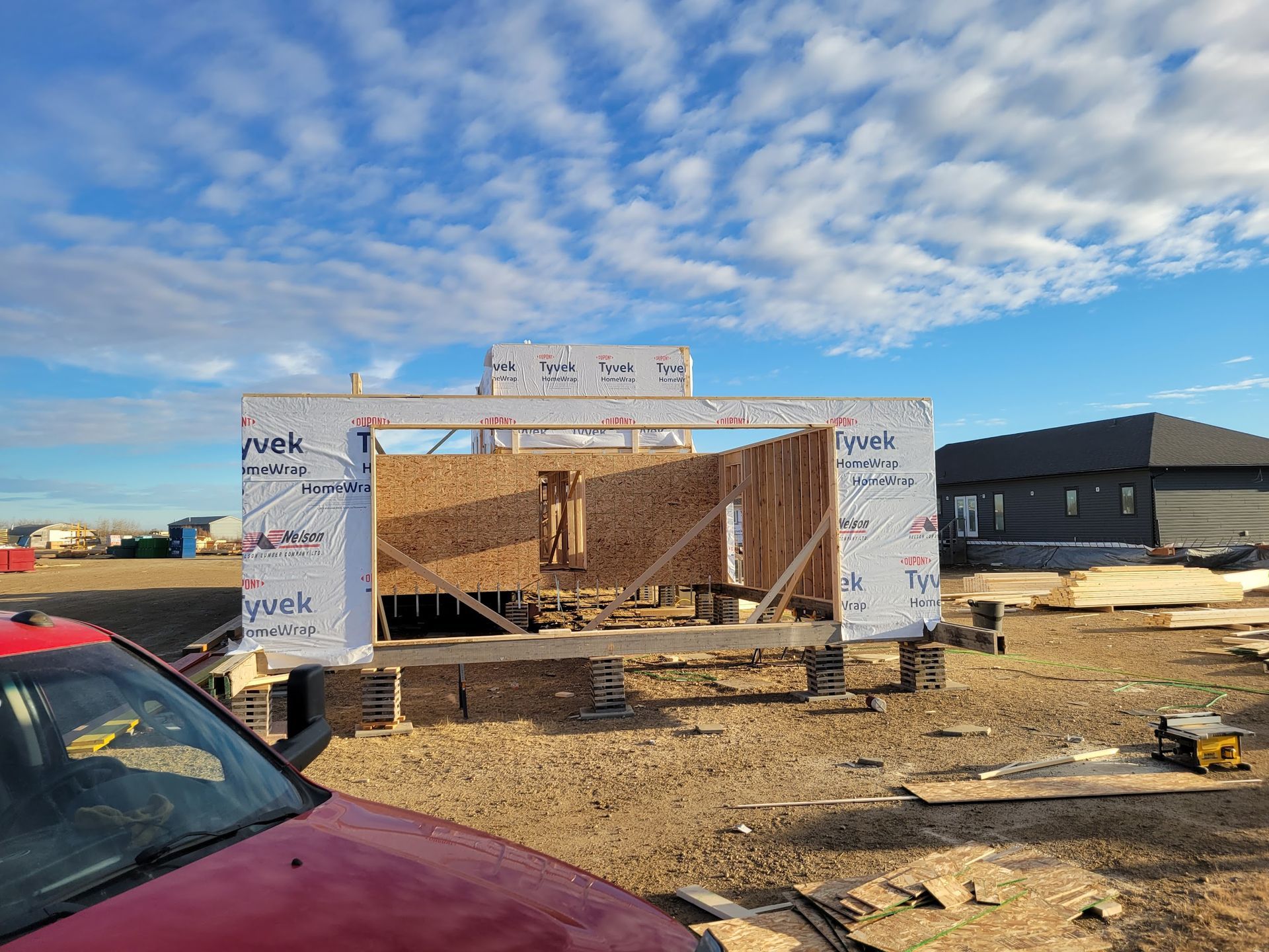 A red car is parked in front of a building under construction.