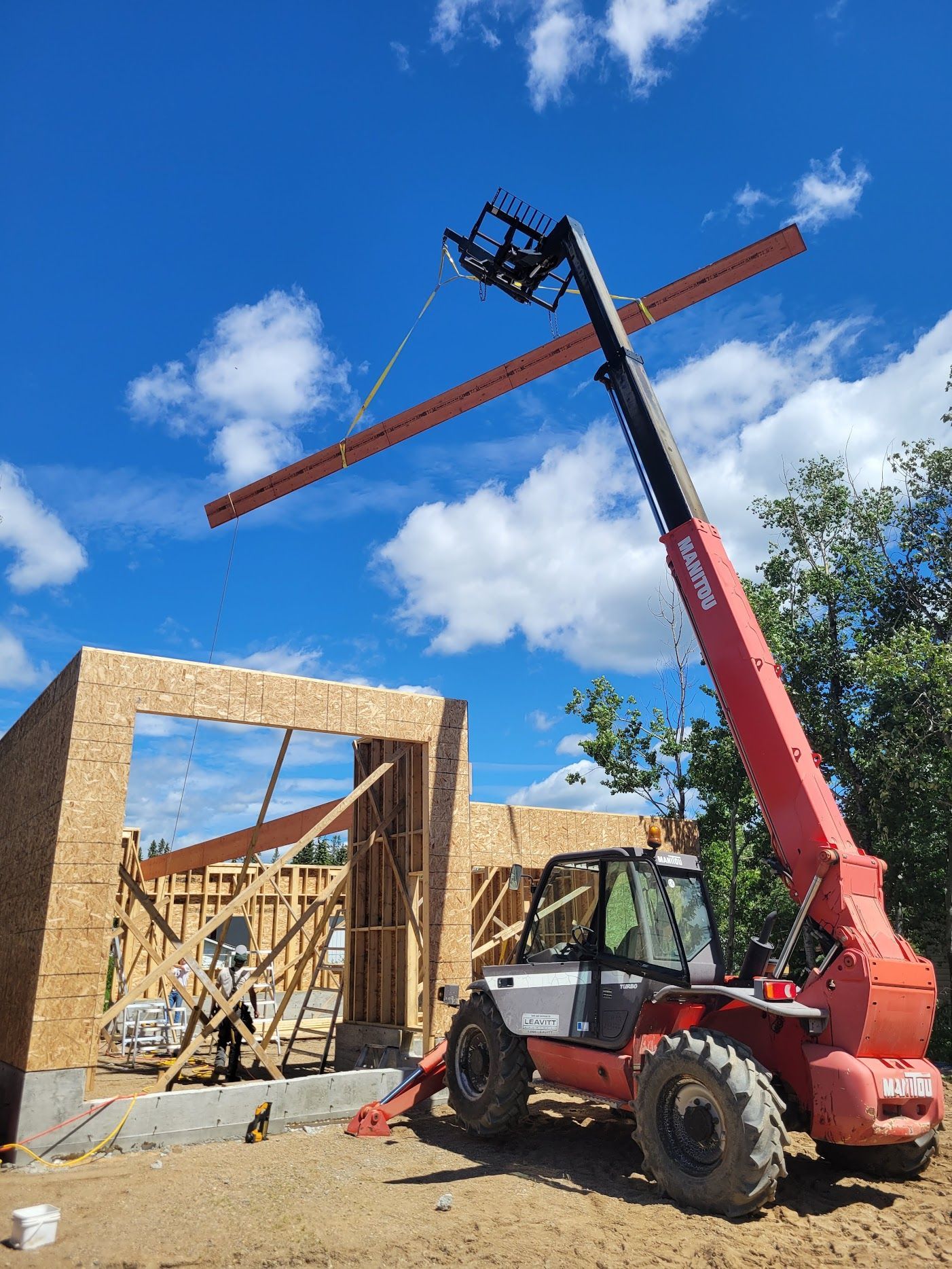 A forklift is lifting a piece of wood in front of a building under construction.