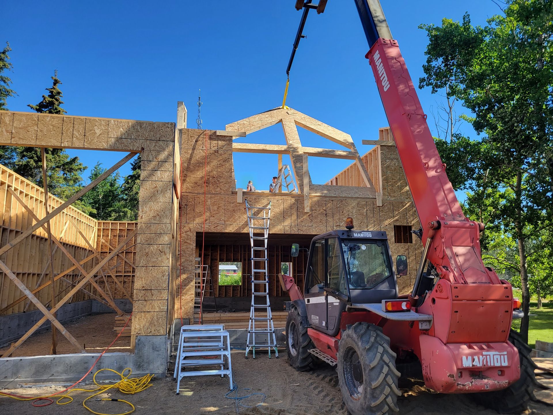 A red crane is lifting a wooden structure in front of a house under construction.