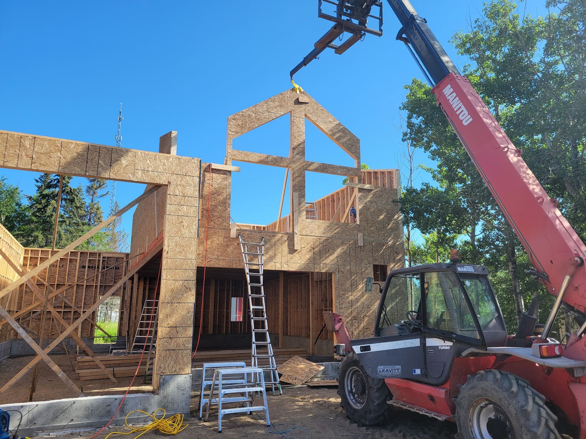 A red forklift is lifting a ladder in front of a house under construction.
