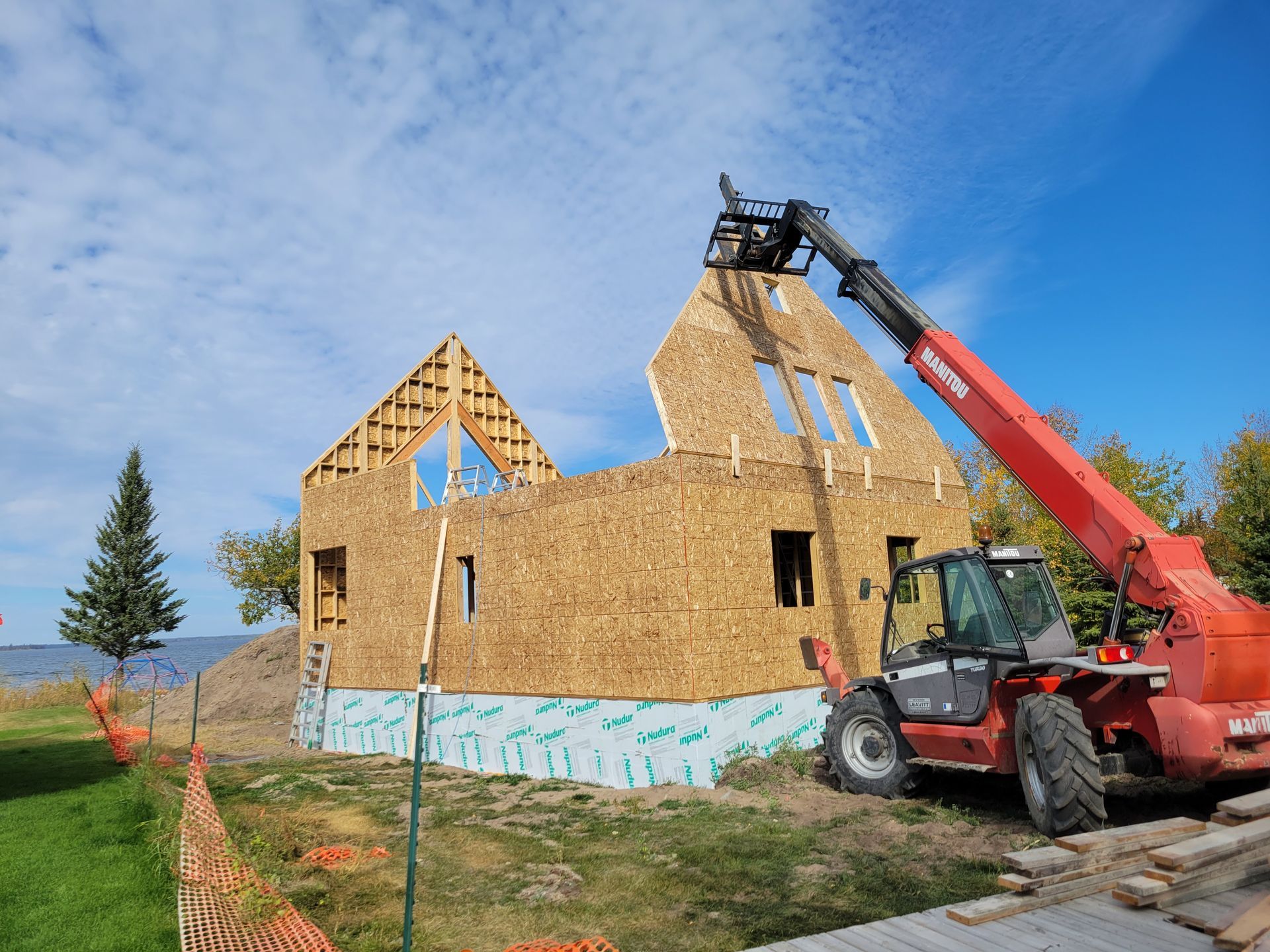 A red forklift is lifting a piece of wood in front of a house under construction.