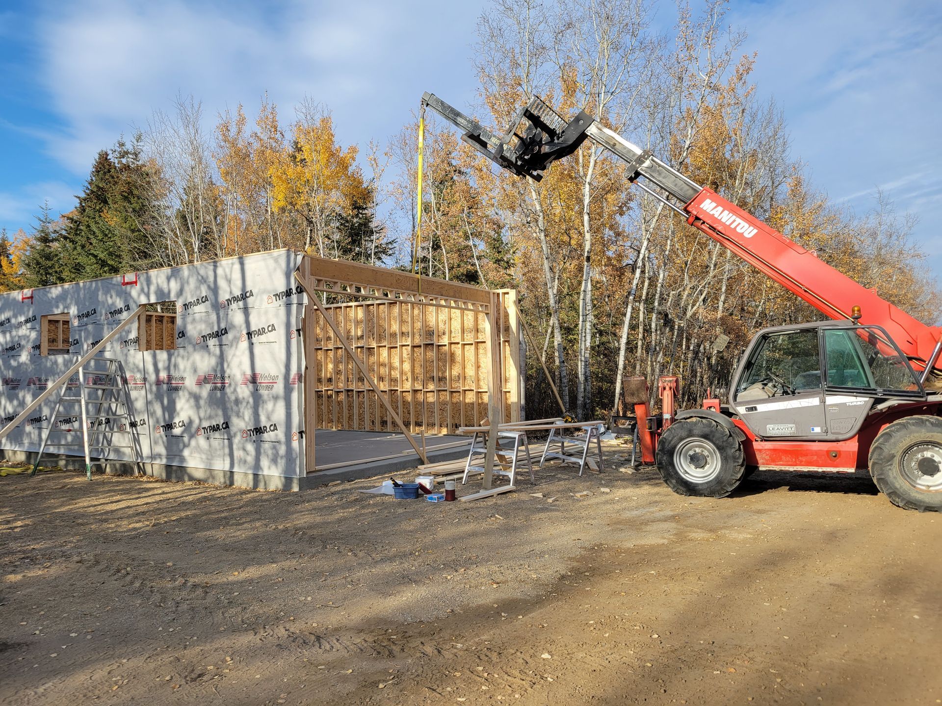 A red forklift is lifting a piece of wood in front of a building under construction.