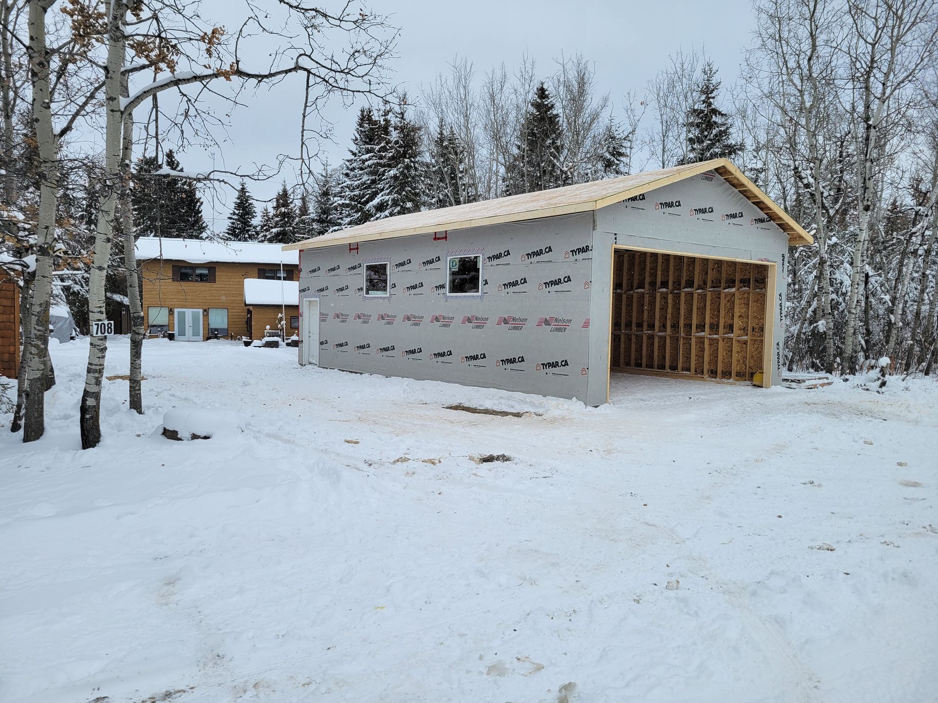 A garage is being built in the snow in front of a house.