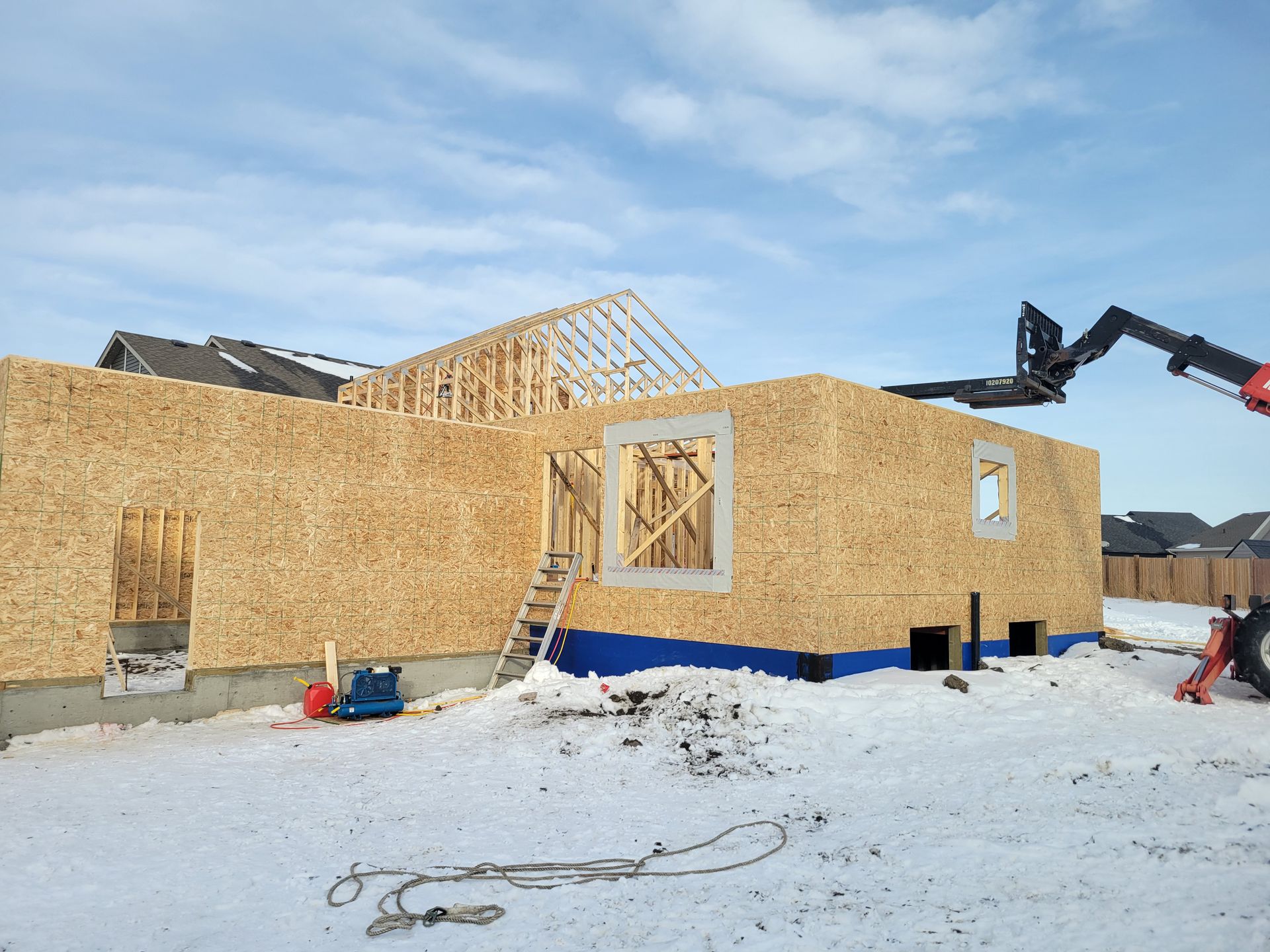 A house is being built in the snow with a forklift in the foreground.