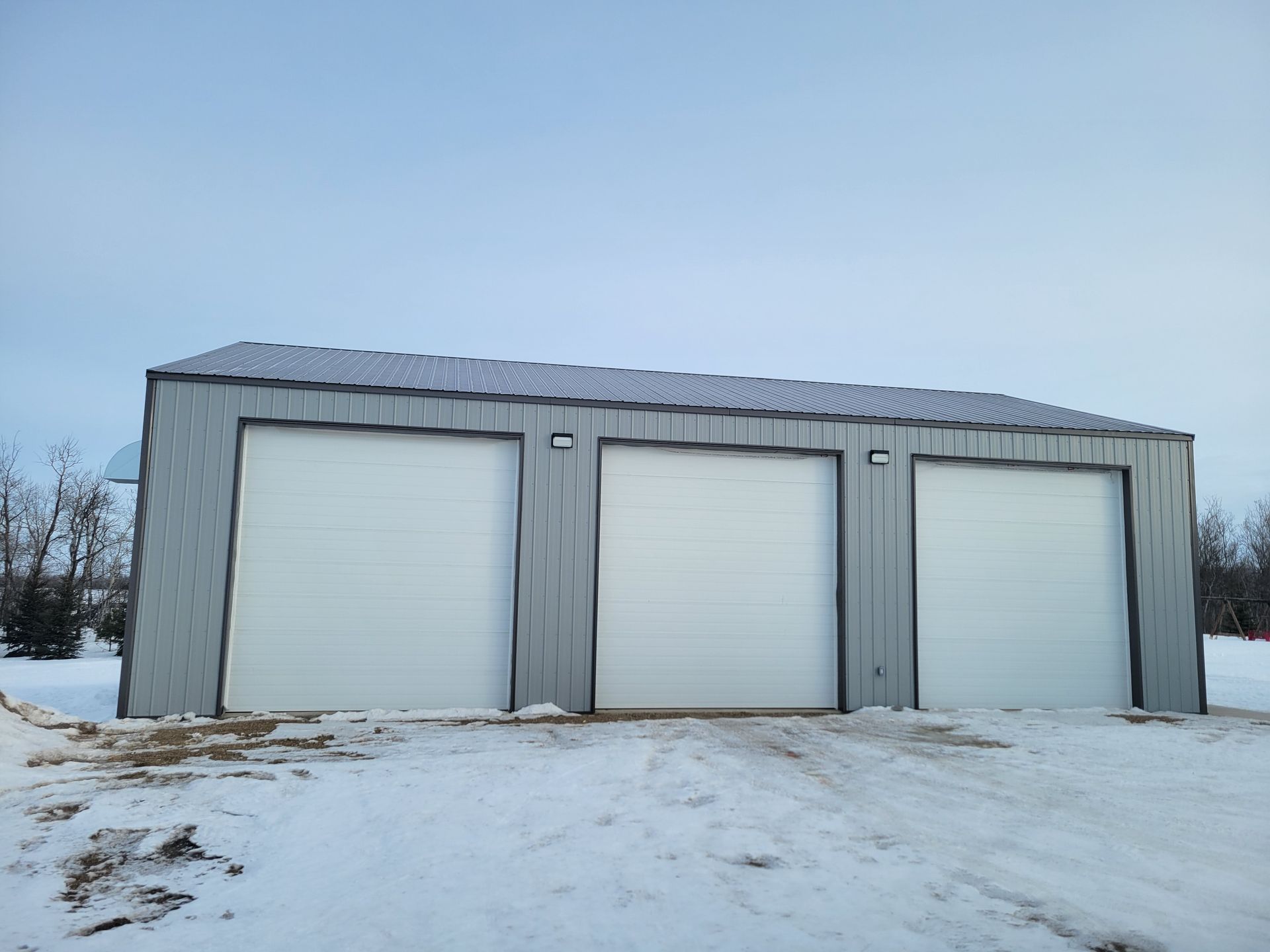 A garage with three garage doors is sitting in the middle of a snowy field.