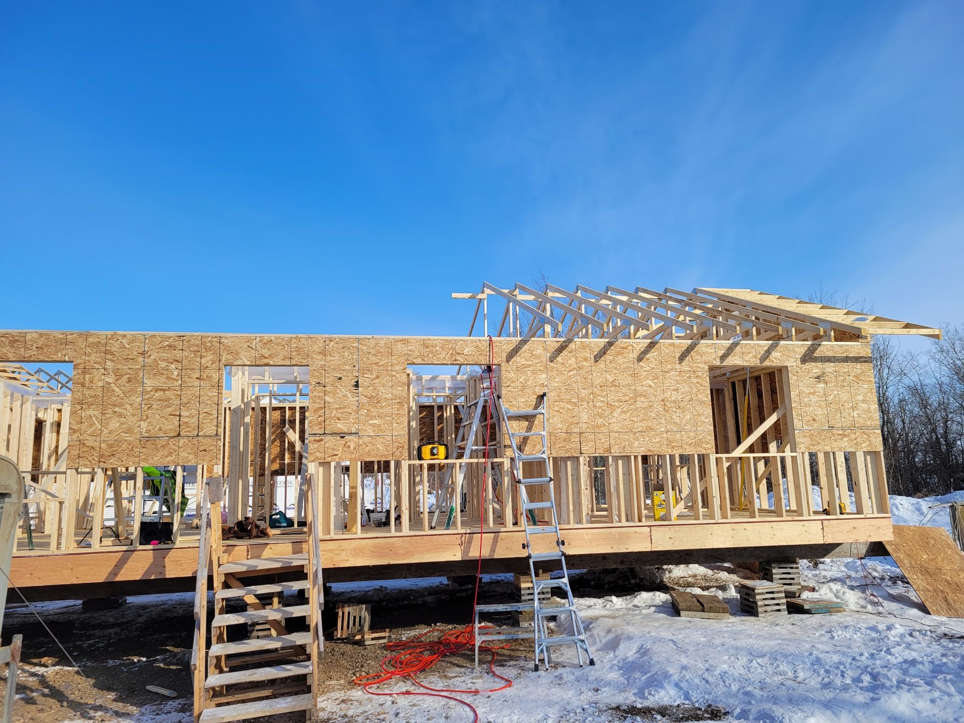 A house is being built in the snow with a blue sky in the background.