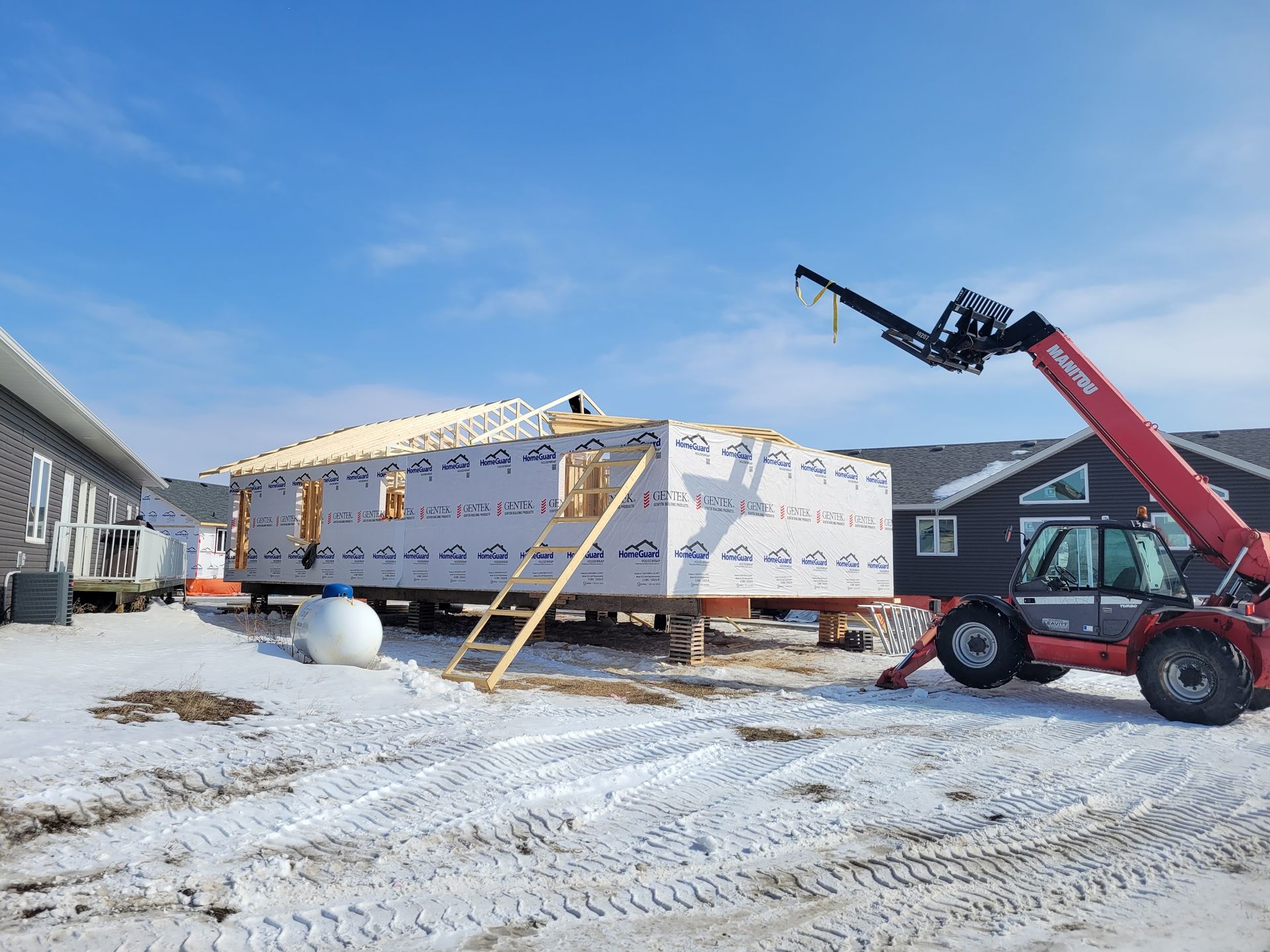 A red forklift is lifting a house in the snow.