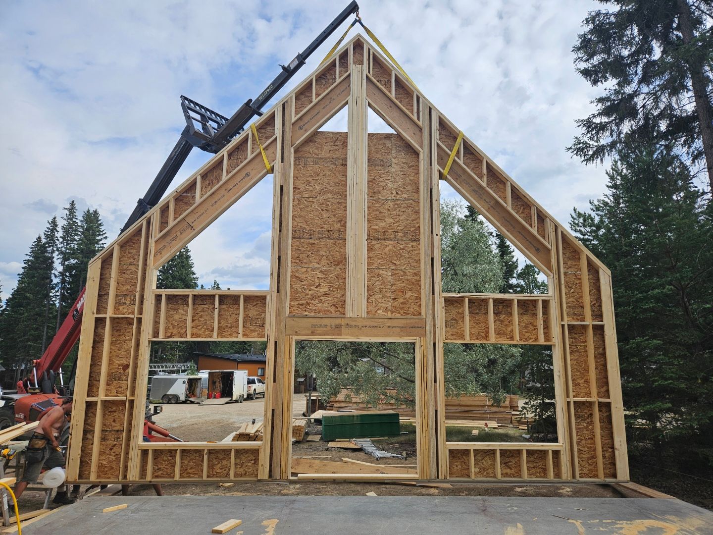Wooden house frame being lifted by a crane during construction, outdoors.