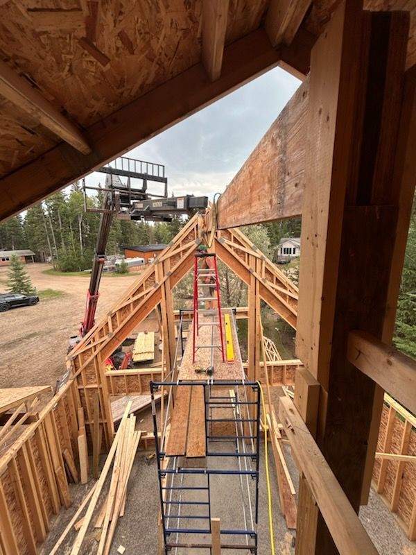 Construction site, view from a wooden structure's interior. Crane overhead, ladders, unfinished framing. Cloudy sky.