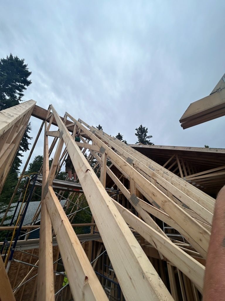 Wooden roof trusses being installed on a building frame under a cloudy sky.