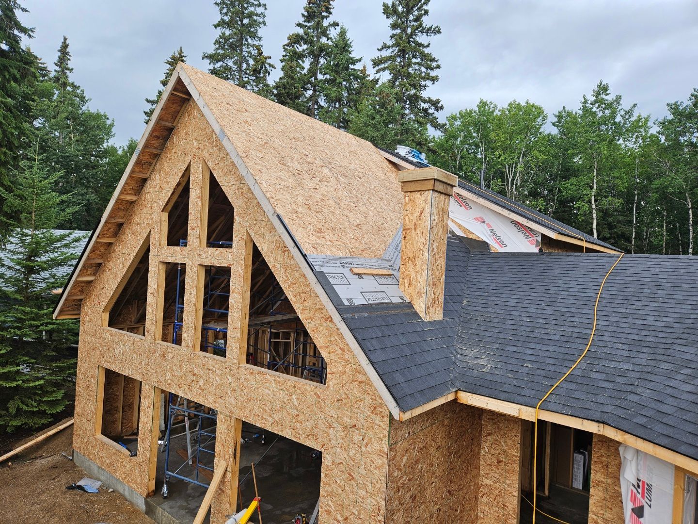 House under construction with exposed wooden frame and partial roofing. Chimney visible.