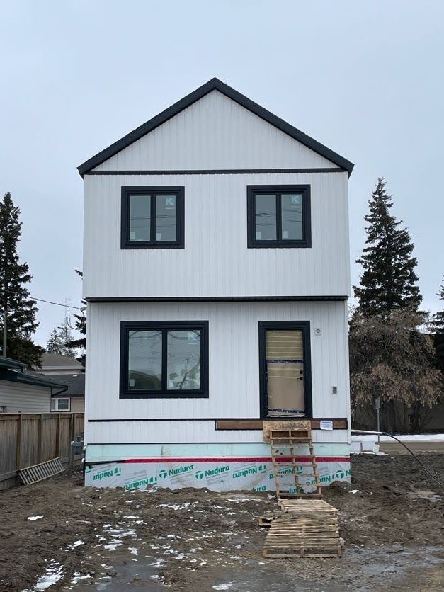Two-story white house with black trim, windows, and roof. Unfinished construction site; wood stairs lead to door.