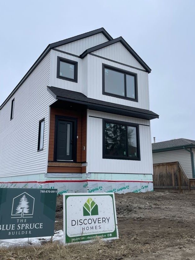 Two-story white house under construction with black trim and windows, two signs in the foreground.