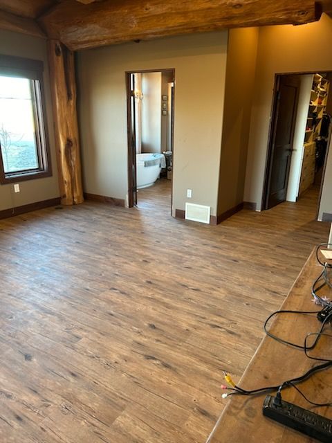 Spacious room with wood-look flooring, neutral walls, and doorways leading to a bathroom and another room.