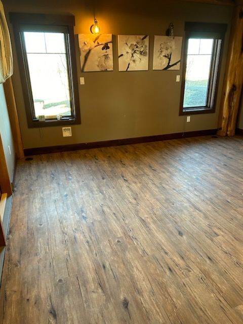 Empty room with wood-look floor, windows with art, and dark green wall.