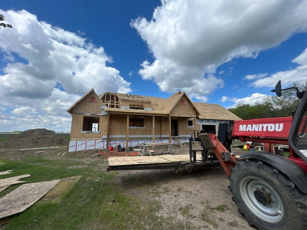 A manitou tractor is parked in front of a house under construction.