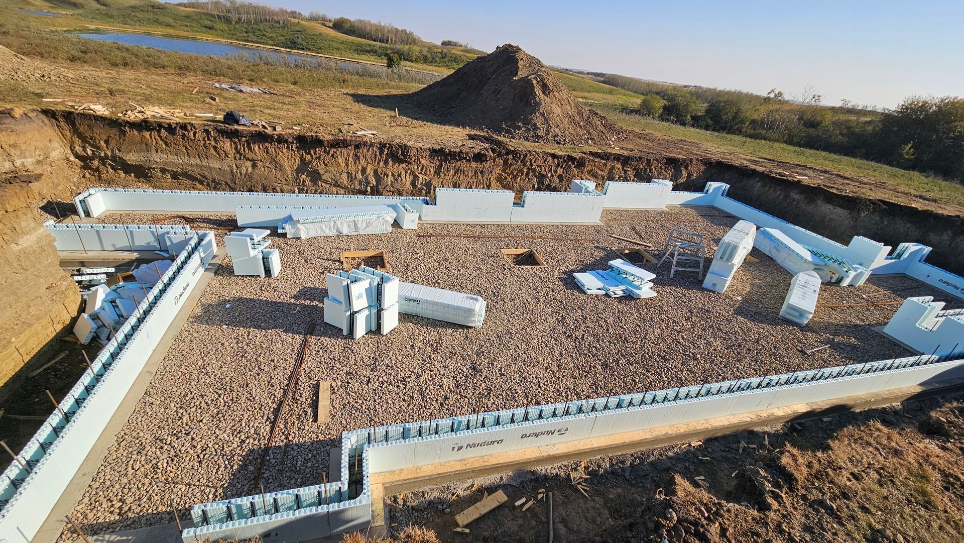 Construction site with foundation blocks laid out in an excavated area. Earth-toned colors.
