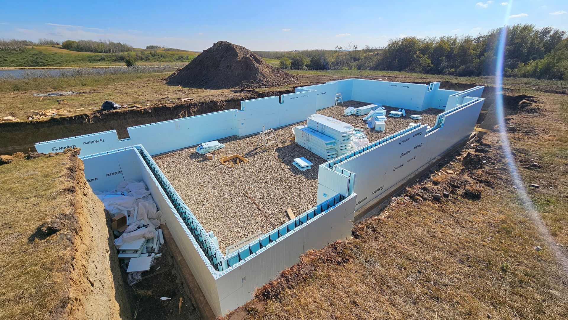 Foundation walls made of blue foam blocks being constructed in a dirt lot.