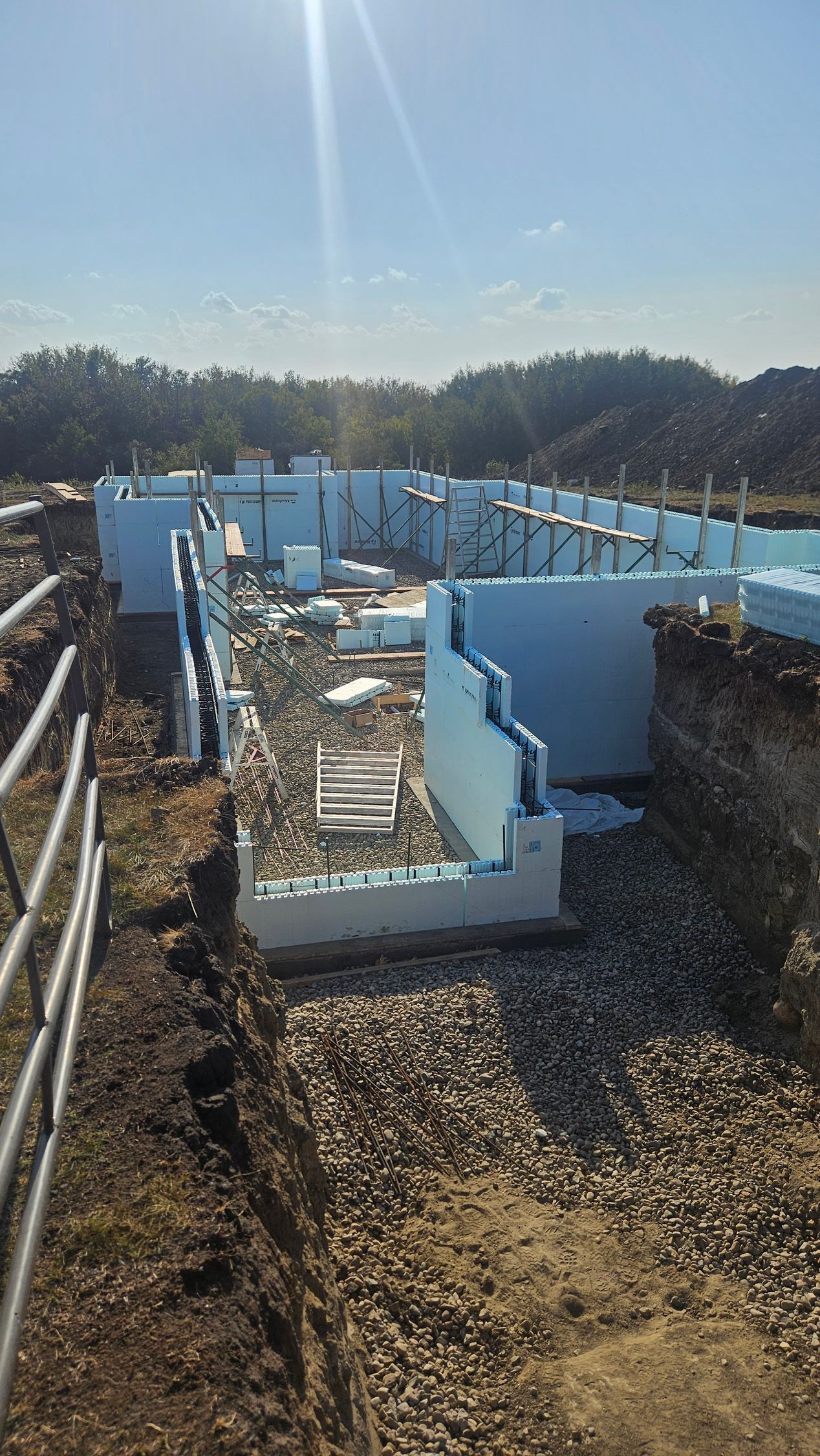 Foundation under construction with blue foam blocks on a gravel base outdoors on a sunny day.