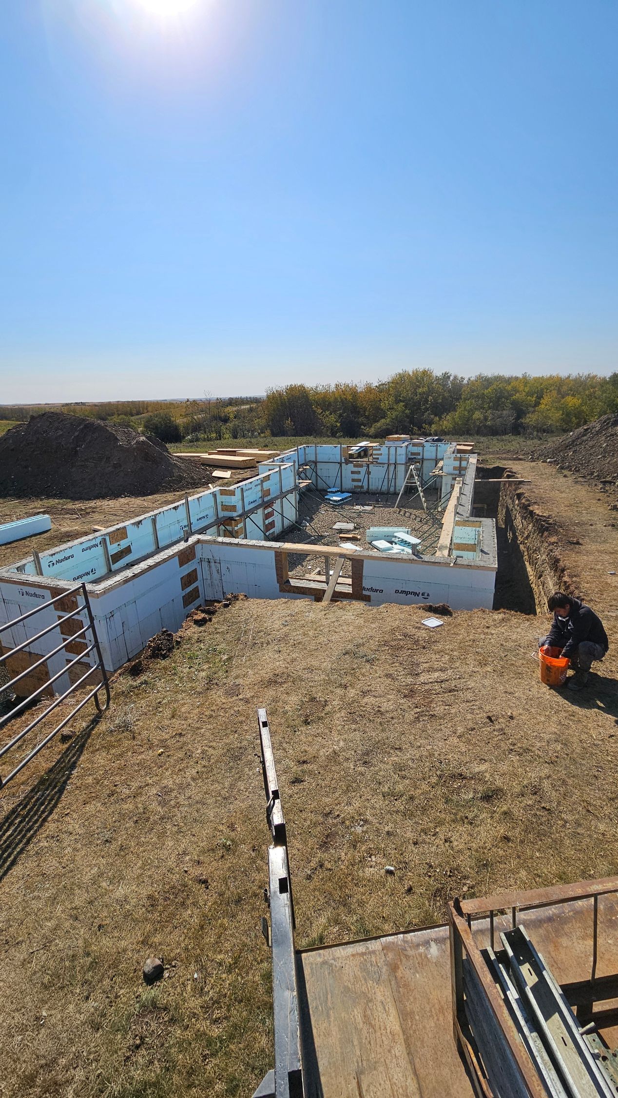Foundation construction site with blue foam walls, brown dirt, and a person kneeling.