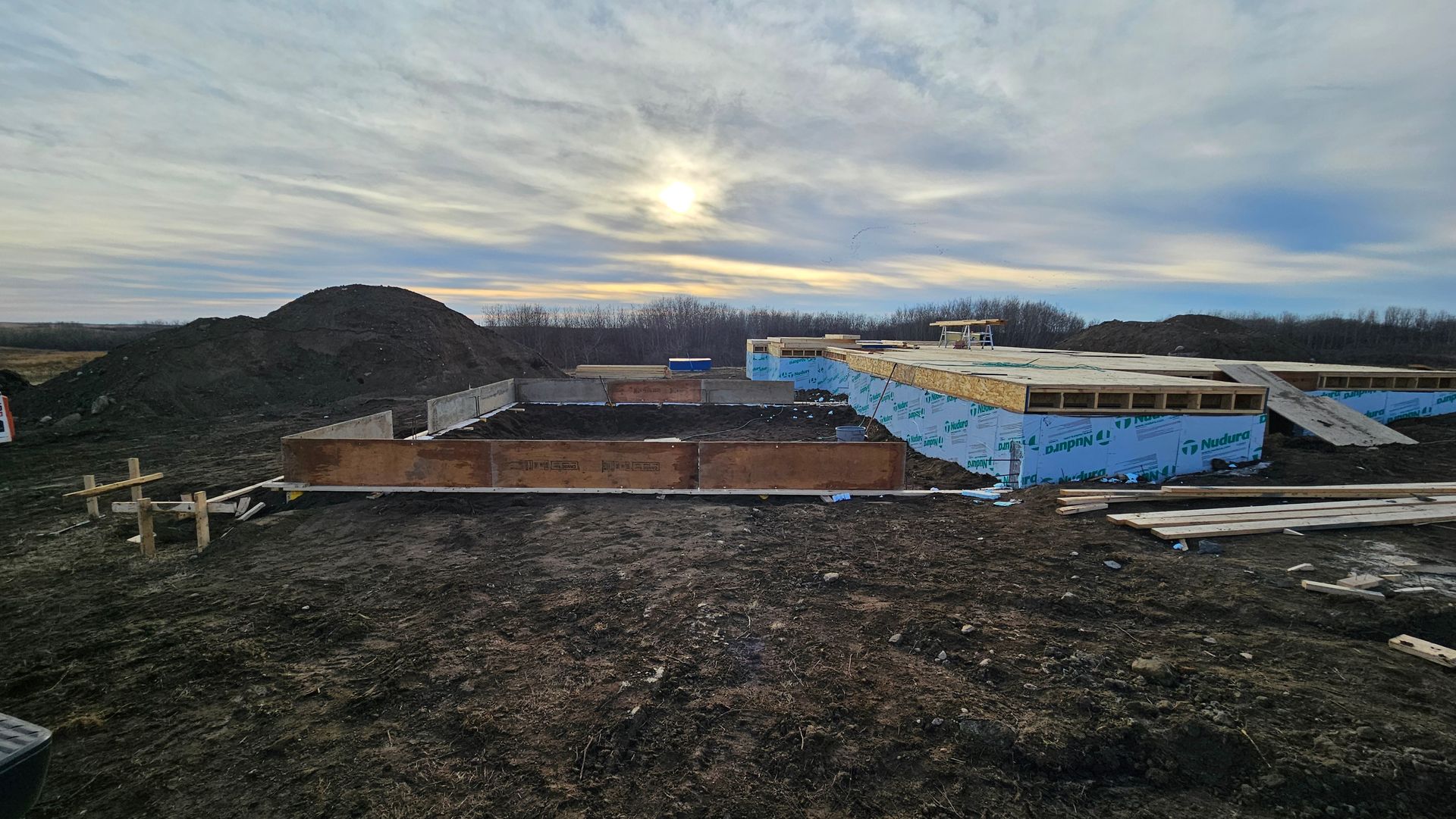 Construction site with wood framing and blue sheathing under a cloudy sky.