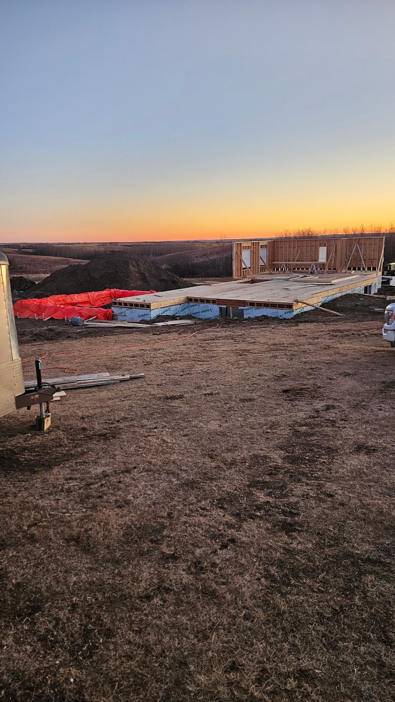Construction materials on a grassy field at sunset. Orange and white stacks of materials, and a building are visible.