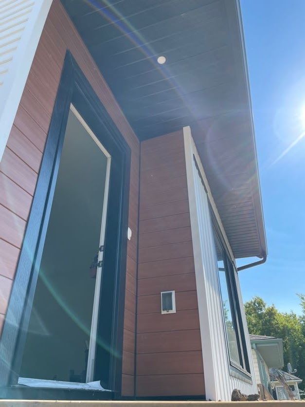 Exterior of a building with brown and white siding, black door frame, and large window.
