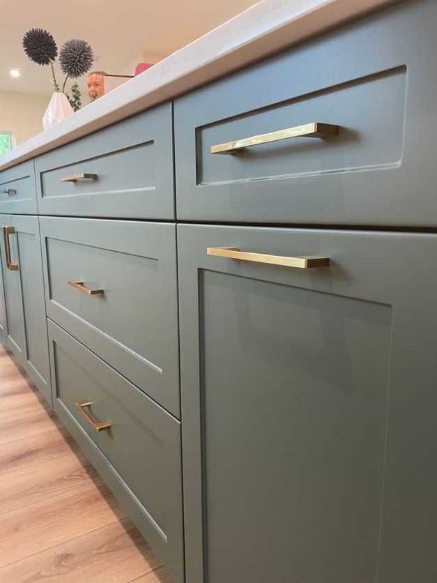 Sage green kitchen cabinets with gold hardware.