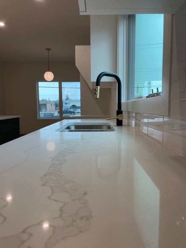Close-up of a kitchen countertop with a black and gold faucet. A sink and a window are visible.