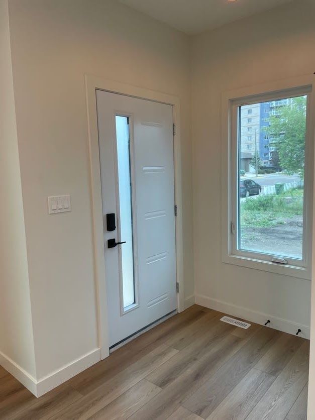 Interior entryway with white door, sidelight, and wood-look flooring.