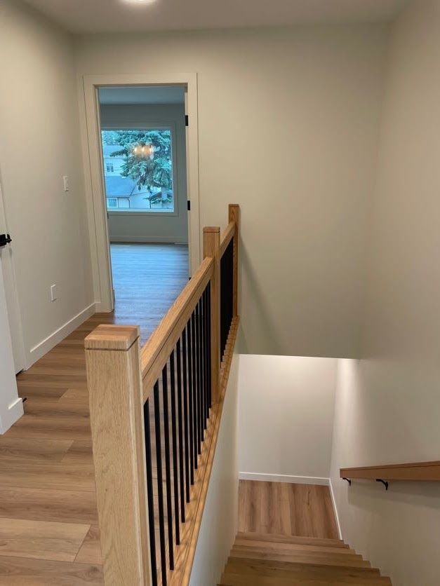 Hallway with wooden staircase and railing, door to room with window.