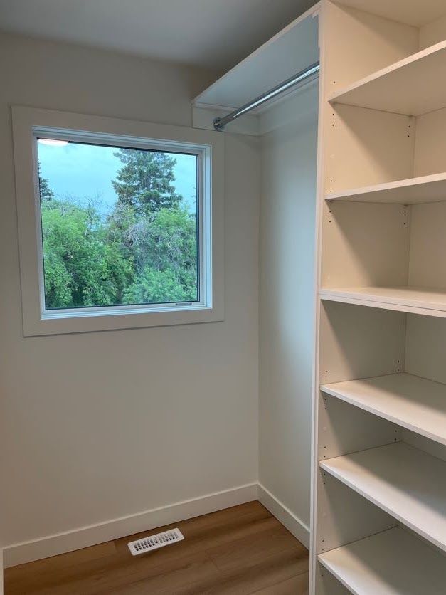 White closet with shelving, a window with a view of greenery, and a clothes rod.