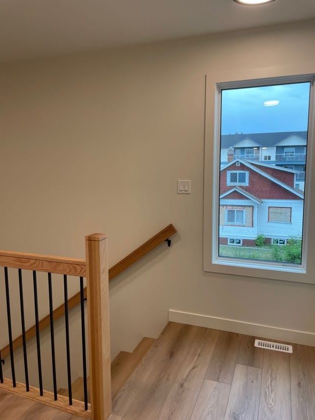 Staircase with light wood steps, railing, and a window with a view of houses outside.