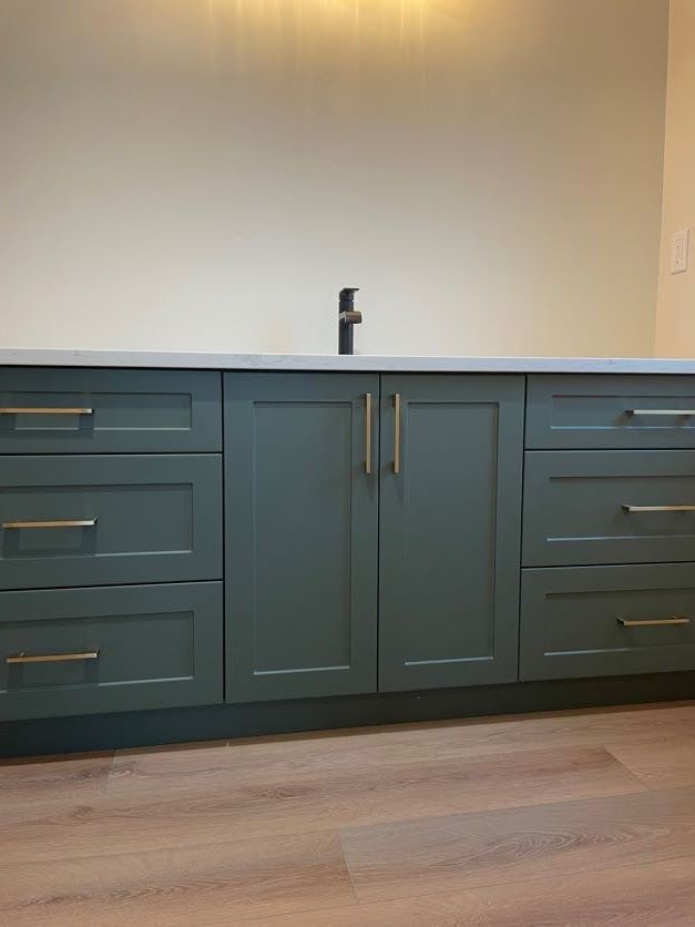 Green bathroom vanity with gold hardware, gray countertop, and black faucet.