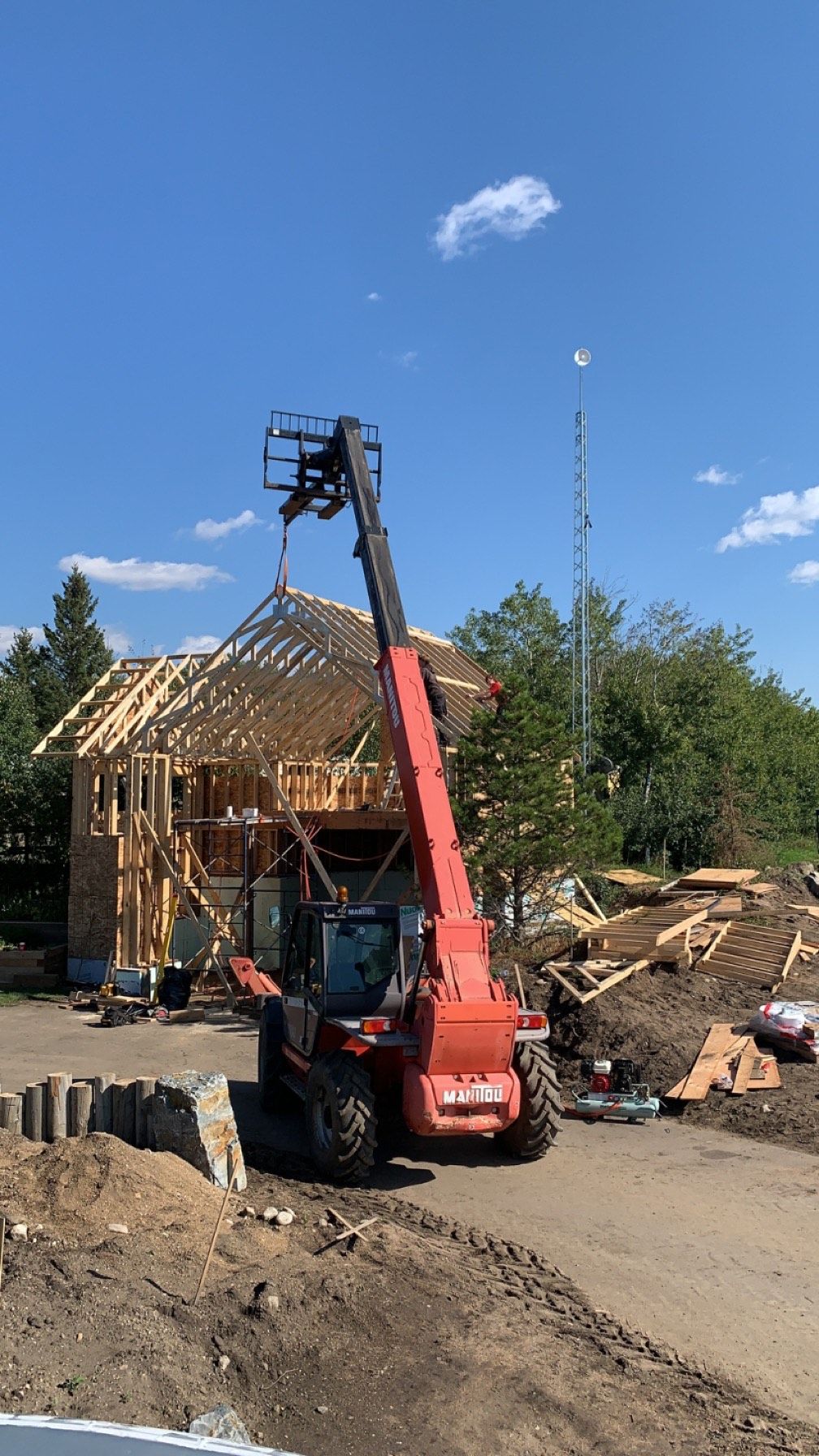 A red forklift is lifting a piece of wood in front of a house under construction.