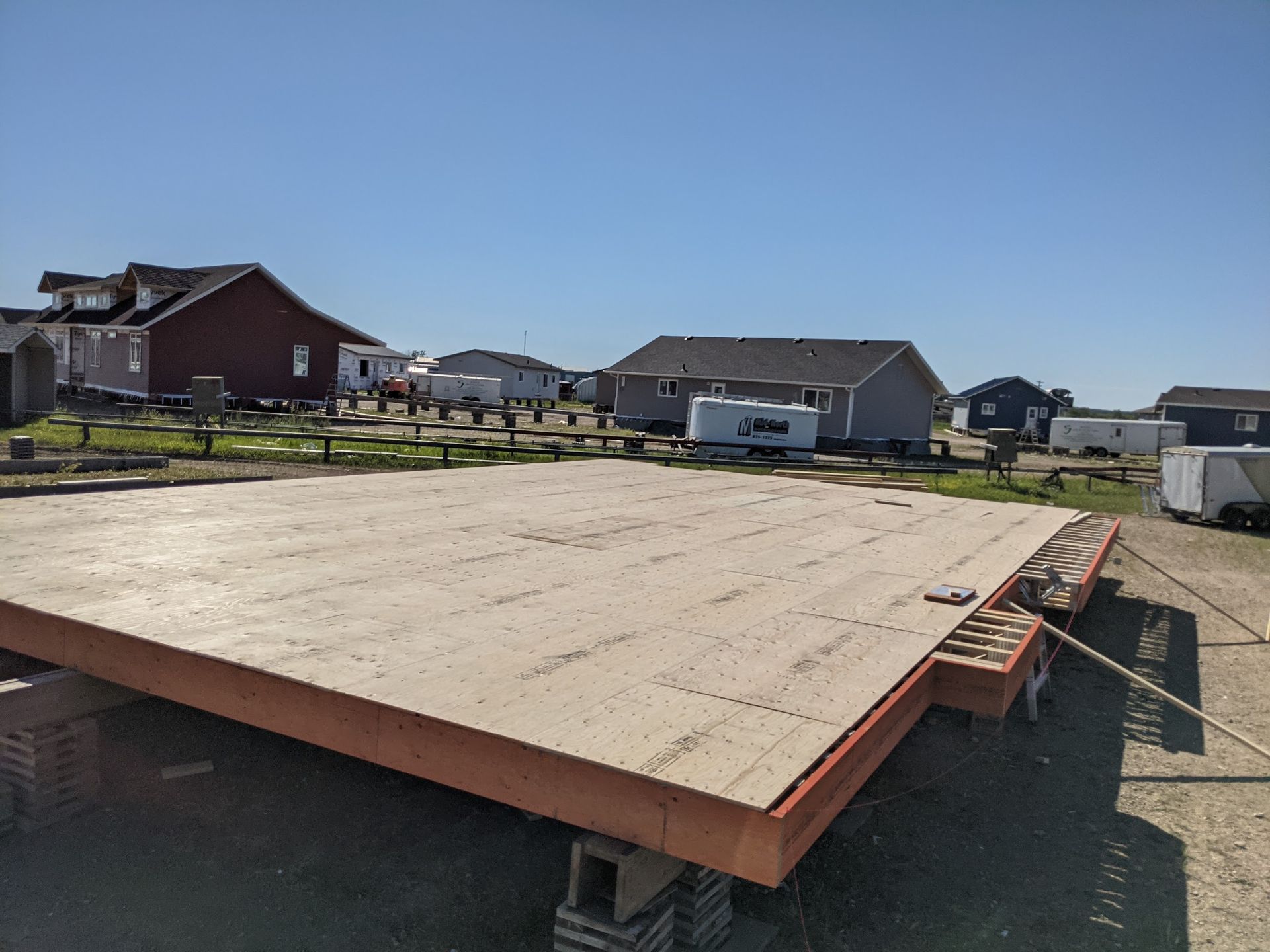A large piece of plywood is sitting in a dirt field with houses in the background