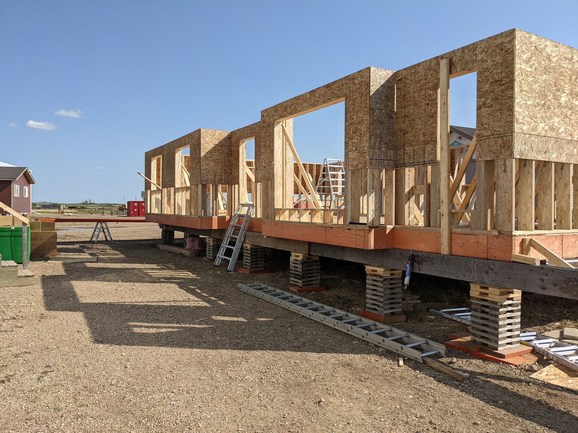 A house is being built in a gravel lot with a ladder in the foreground.