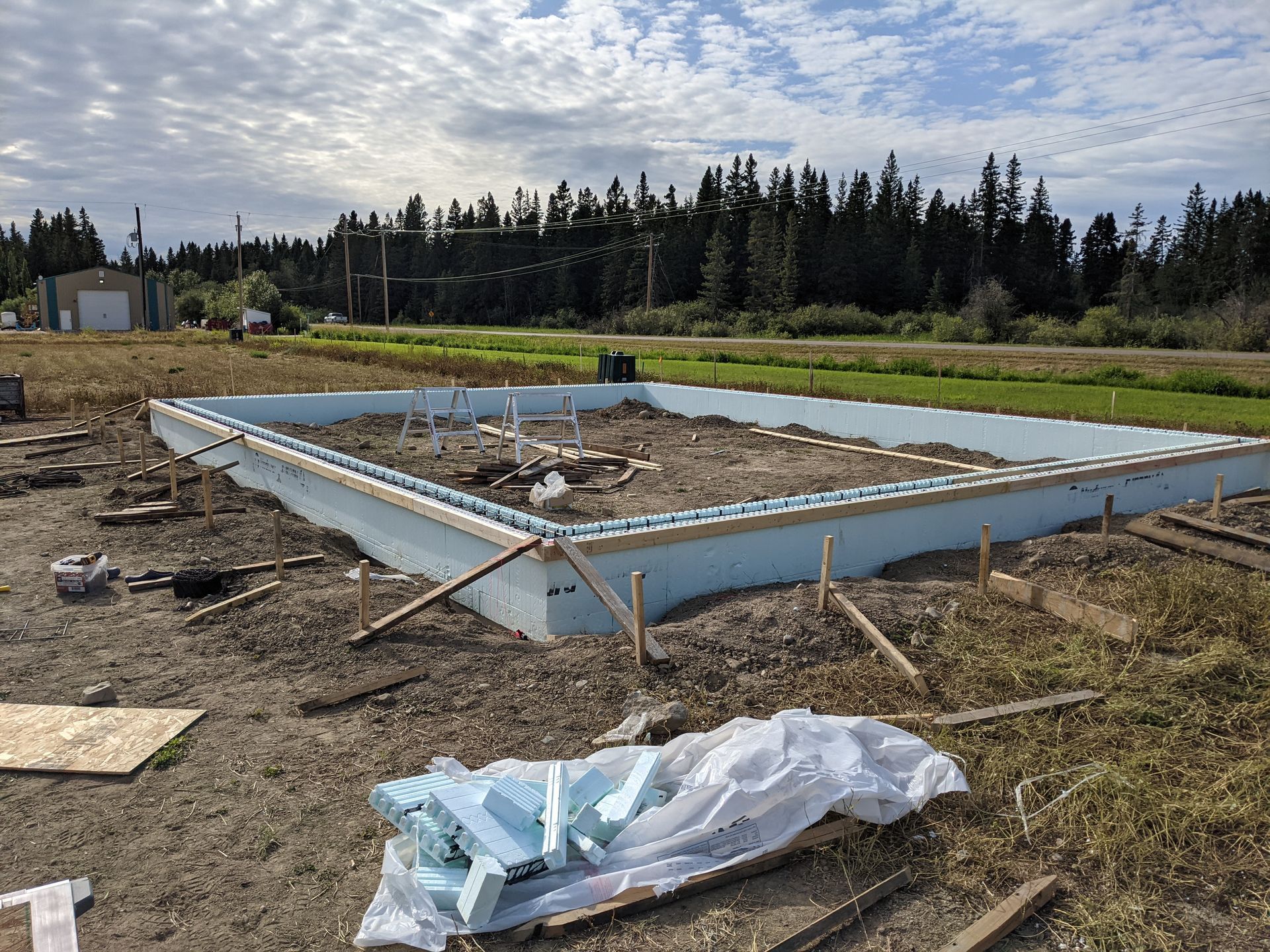 Foundation of a building under construction, blue foam walls, on a dirt lot, rural setting.