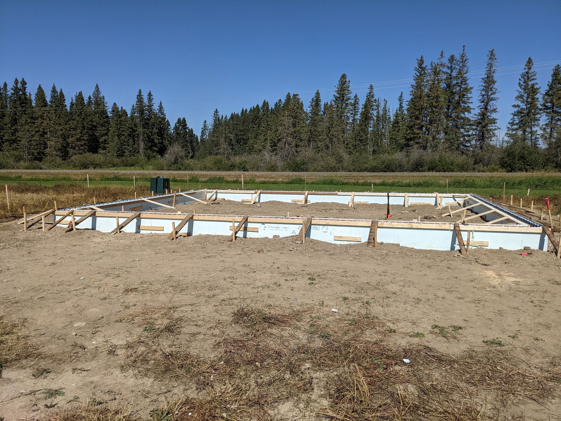 A concrete foundation is being built in a field with trees in the background