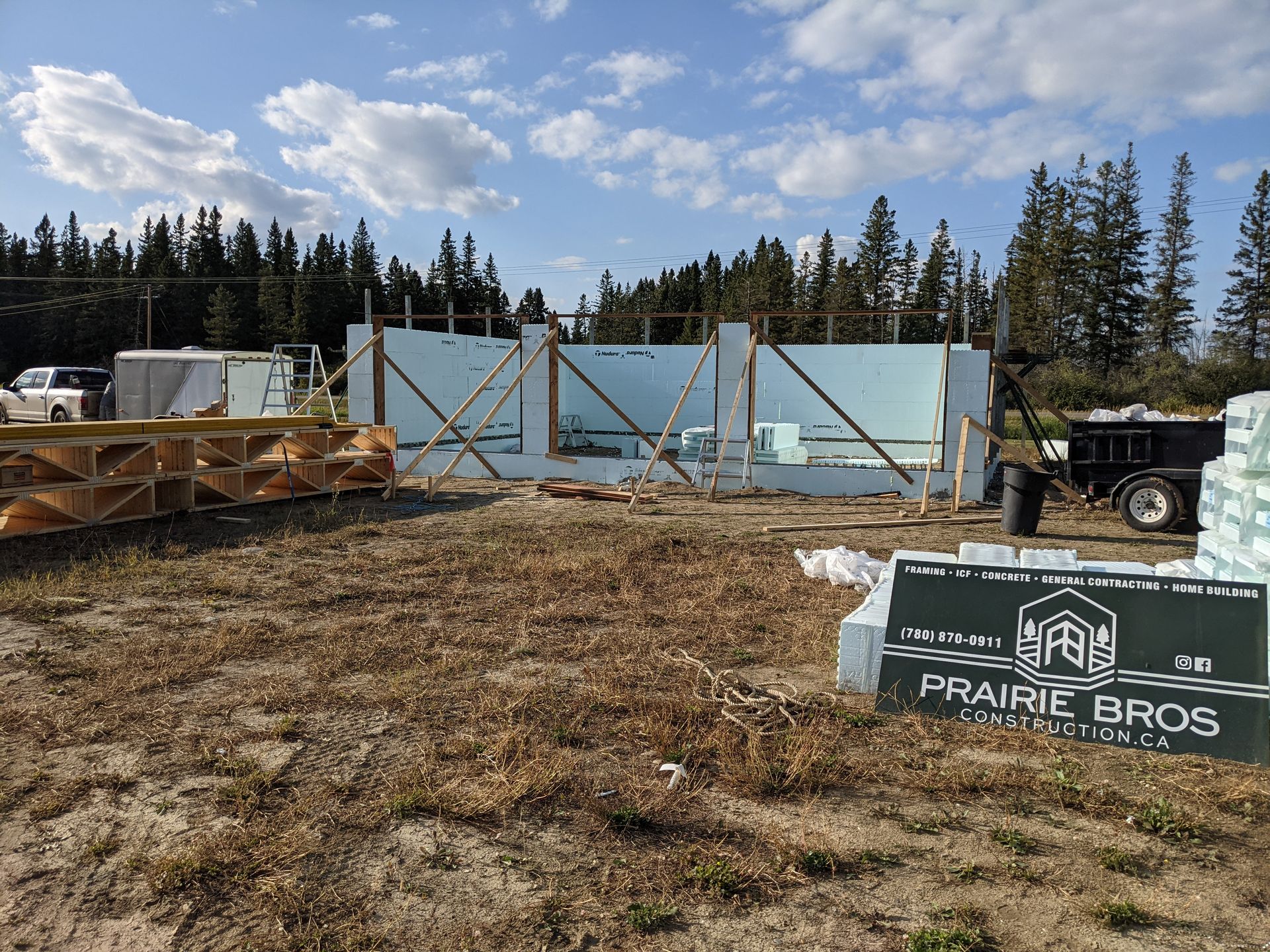 Construction site with blue foam walls, wood supports, and stacked materials under a partly cloudy sky.