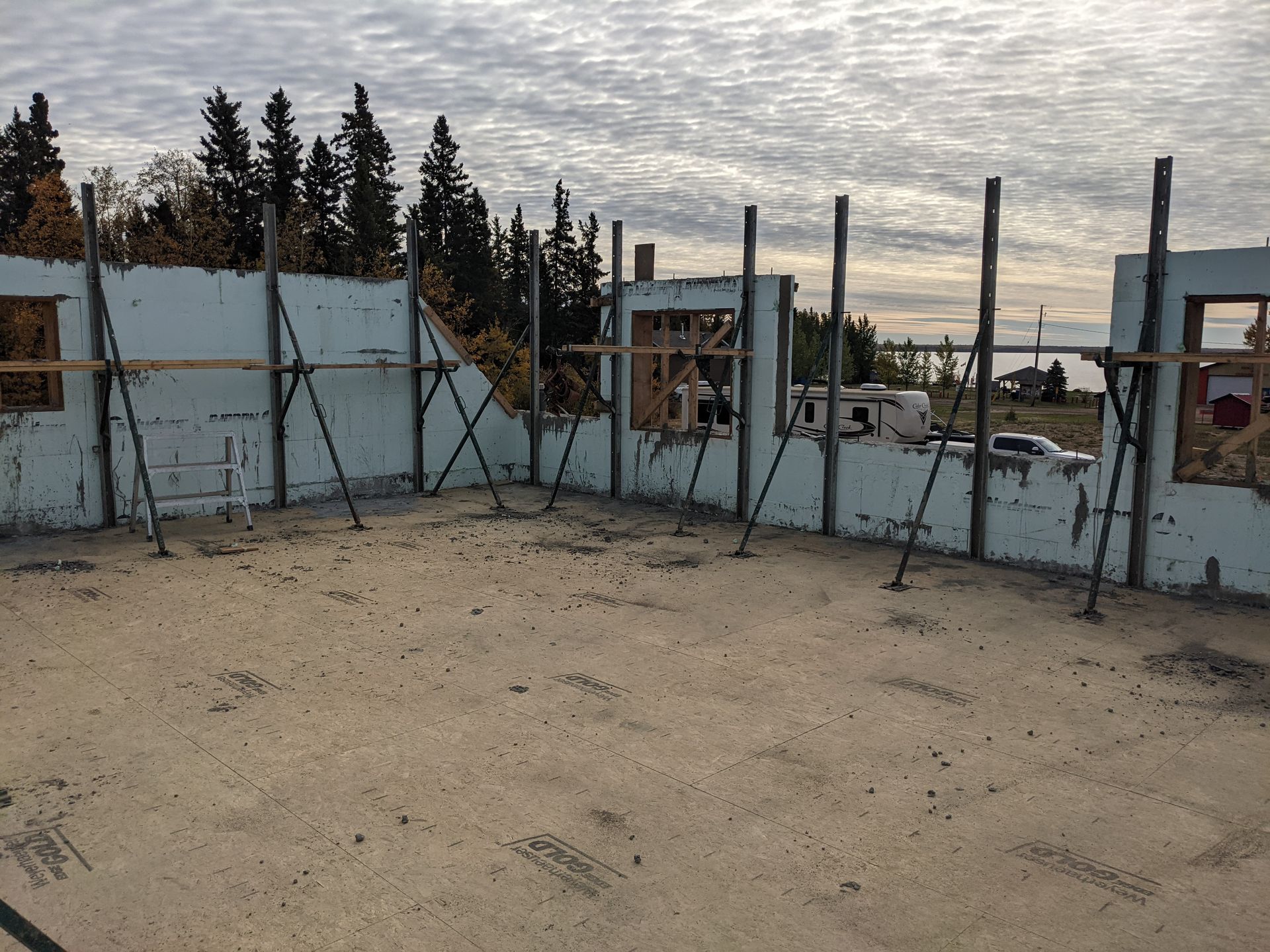 Exterior view of a building under construction. Foam walls supported by metal braces on a concrete foundation, cloudy sky.