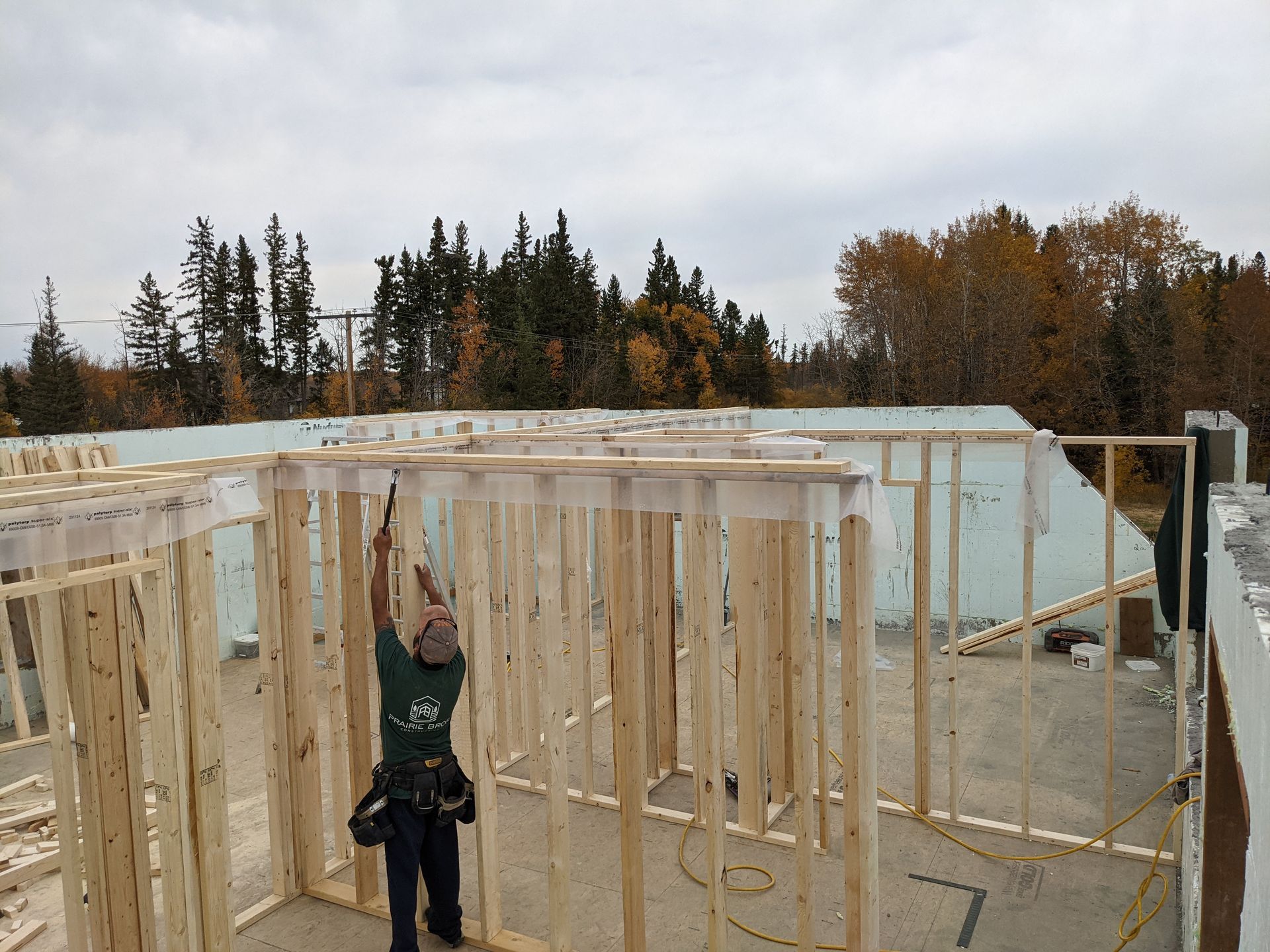 Construction worker framing walls on a building site, surrounded by ICF blocks and wood, under an overcast sky.