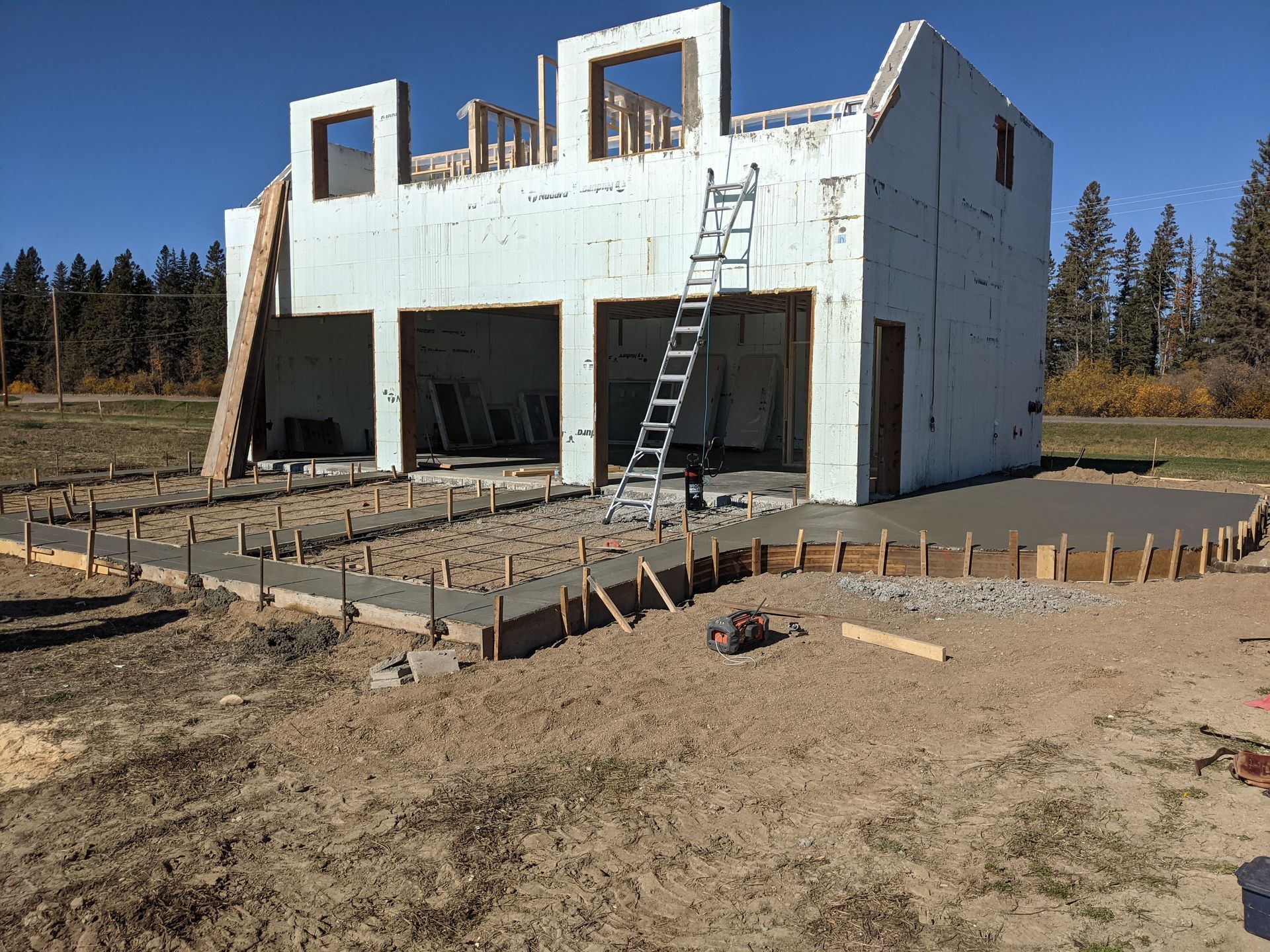 Garage under construction with concrete foundation, wooden frame, and ladder.