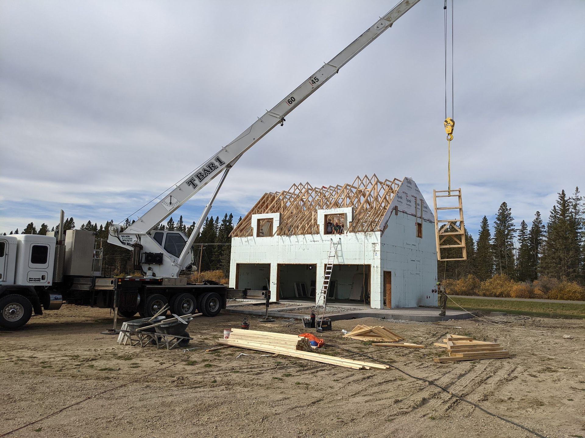 A crane is lifting a piece of wood in front of a house under construction.