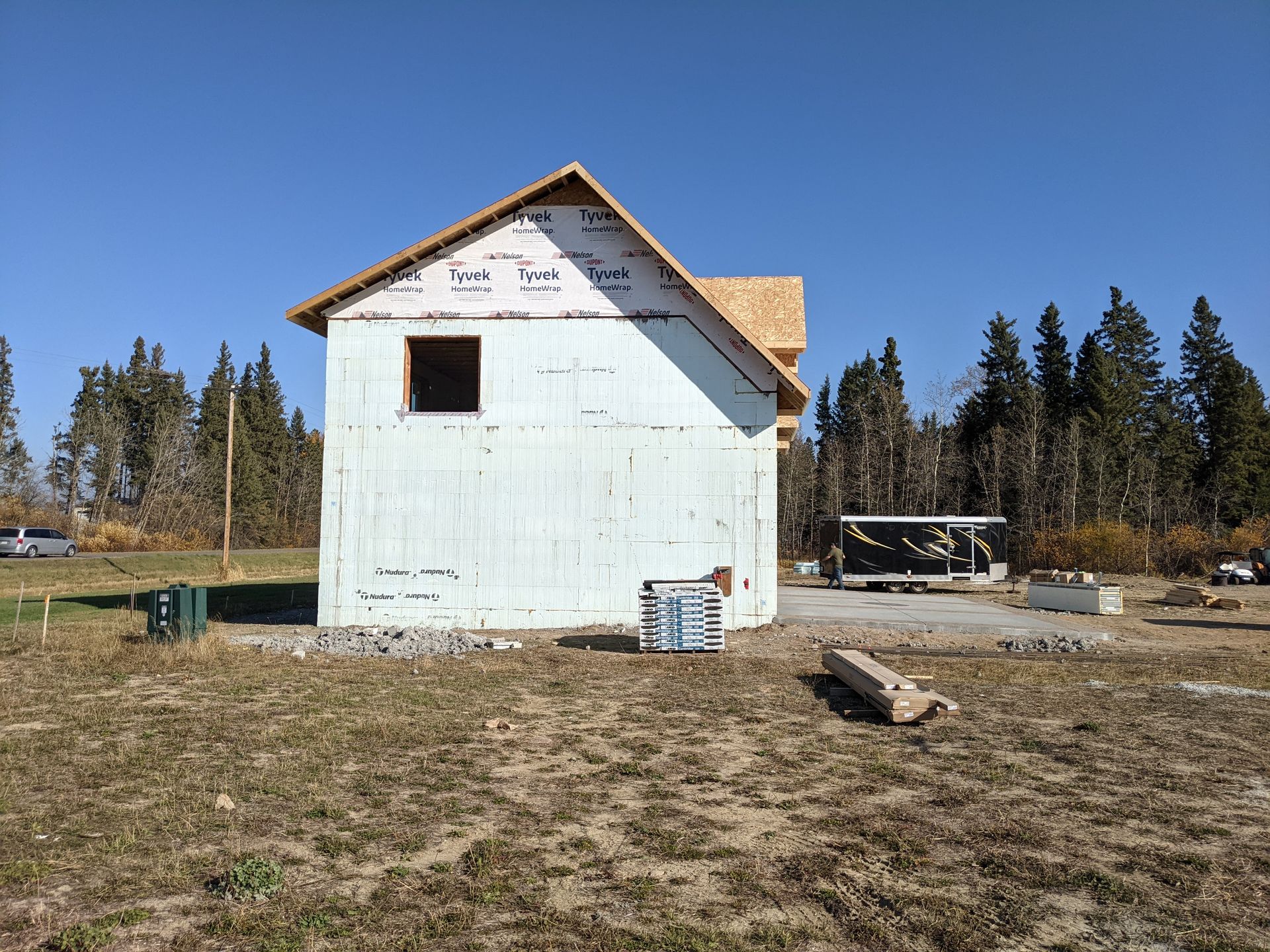 Construction of a small house with white siding and a wood-framed roof against a blue sky, in a field.